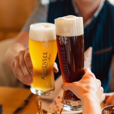 Das Hotel Karlwirt: herzlich willkommen! Zwei Personen stoßen mit einem hellen und einem dunklen Achensee Bier an