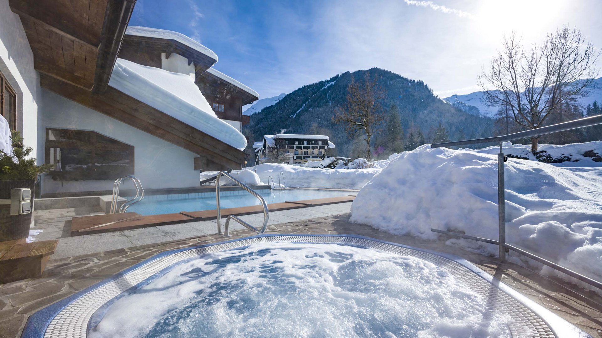 Das Hotel Karlwirt: herzlich willkommen! Outdoor-Whirlpool und Pool neben schneebedecktem Haus mit Blick auf verschneite Berge