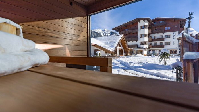 Das Hotel Karlwirt: herzlich willkommen! Blick aus Sauna auf verschneiten Hotelgarten und Berge bei Sonnenschein