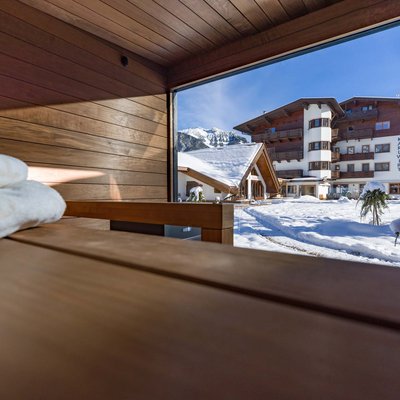 Das Hotel Karlwirt: herzlich willkommen! Blick aus Sauna auf verschneiten Hotelgarten und Berge bei Sonnenschein