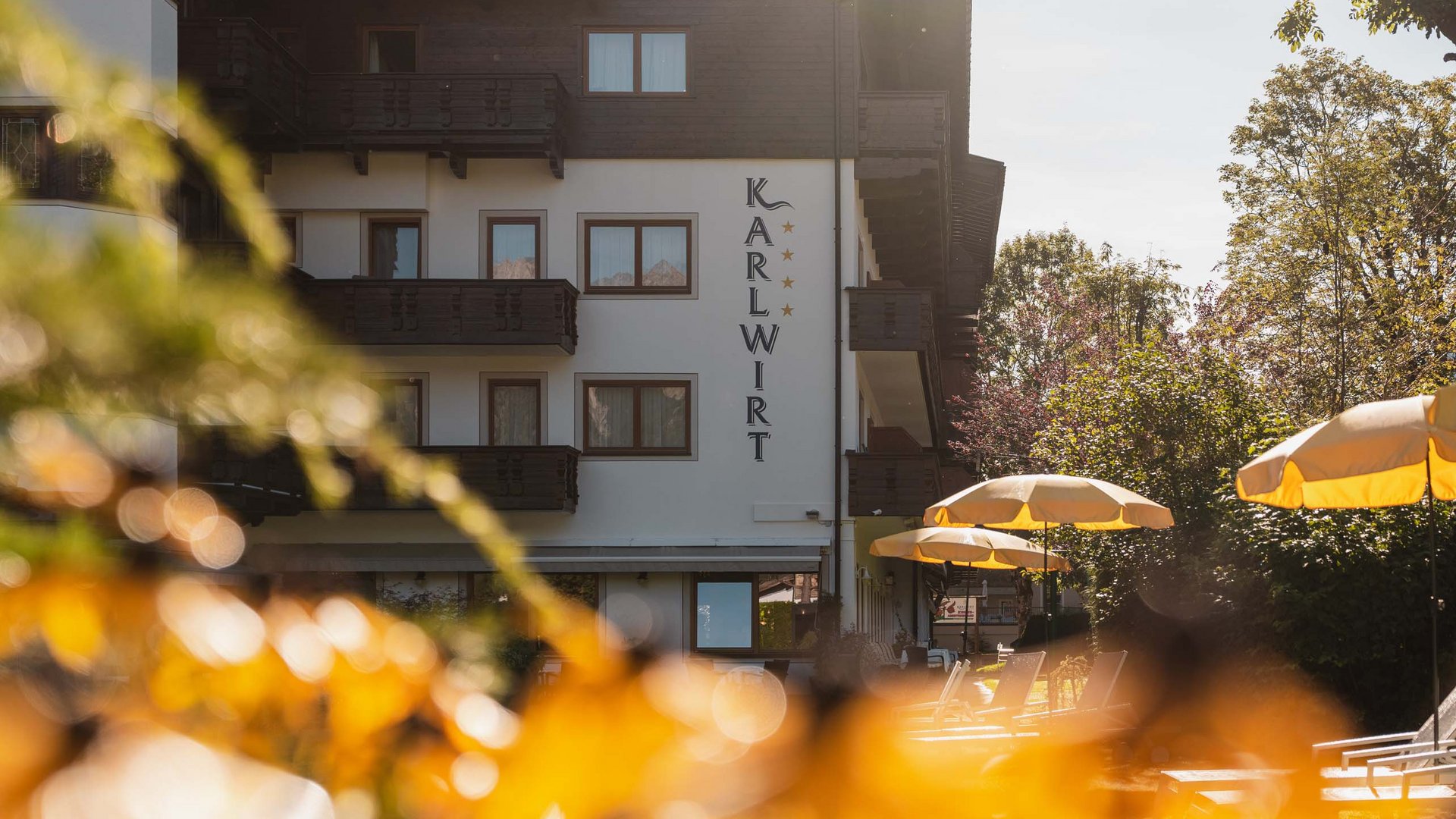 Das Hotel Karlwirt: herzlich willkommen! Hotel Karlwirt mit Sonnenschirmen und Bäumen im Sonnenlicht