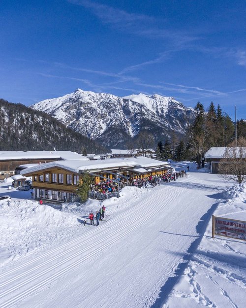 Das Hotel Karlwirt: herzlich willkommen! Winterlandschaft mit verschneiten Bergen und Skihütte mit Menschen auf Sonnenterrasse