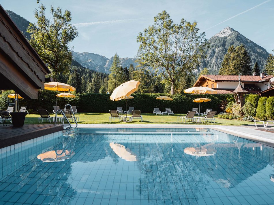 Das Hotel Karlwirt: herzlich willkommen! Pool mit gelben Sonnenschirmen vor Berglandschaft und Haus