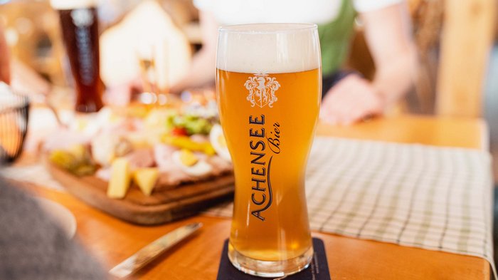 The Karlwirt’s Achenseebier A glass of Achensee beer on a table with a snack platter in the background
