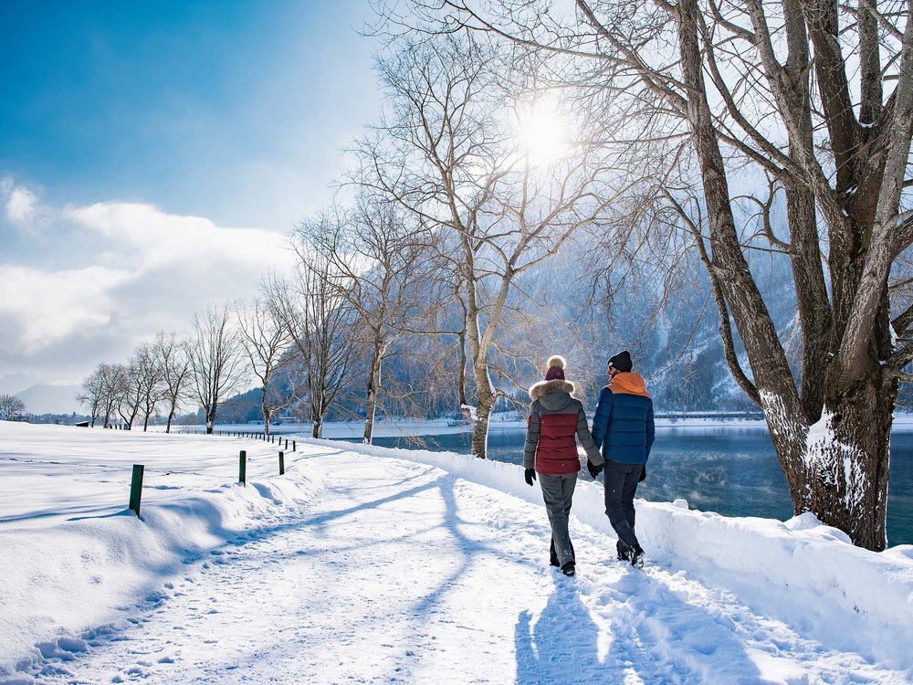 Skiing at Lake Achensee and more Couple holding hands walking on snowy path by a lake in winter