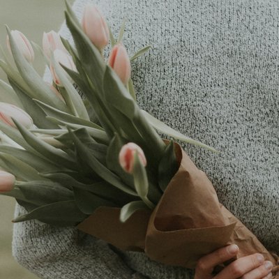 Das Hotel Karlwirt: herzlich willkommen! Frau mit roten Haaren hält blühenden Tulpenstrauß hinter Rücken im Freien