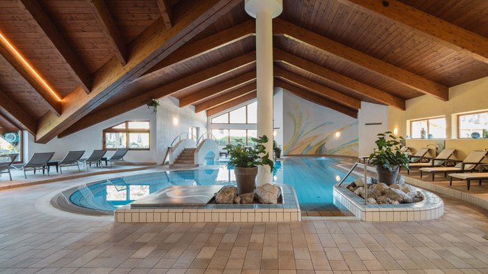 Das Hotel Karlwirt: herzlich willkommen! Innenansicht eines Schwimmbads mit Holzdecke, Liegestühlen und Pflanzen