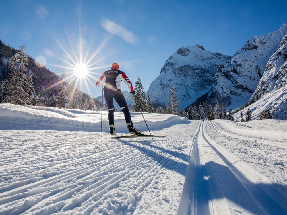 Skiing at Lake Achensee and more Cross-country skier on snowy trail with mountains and sun in background