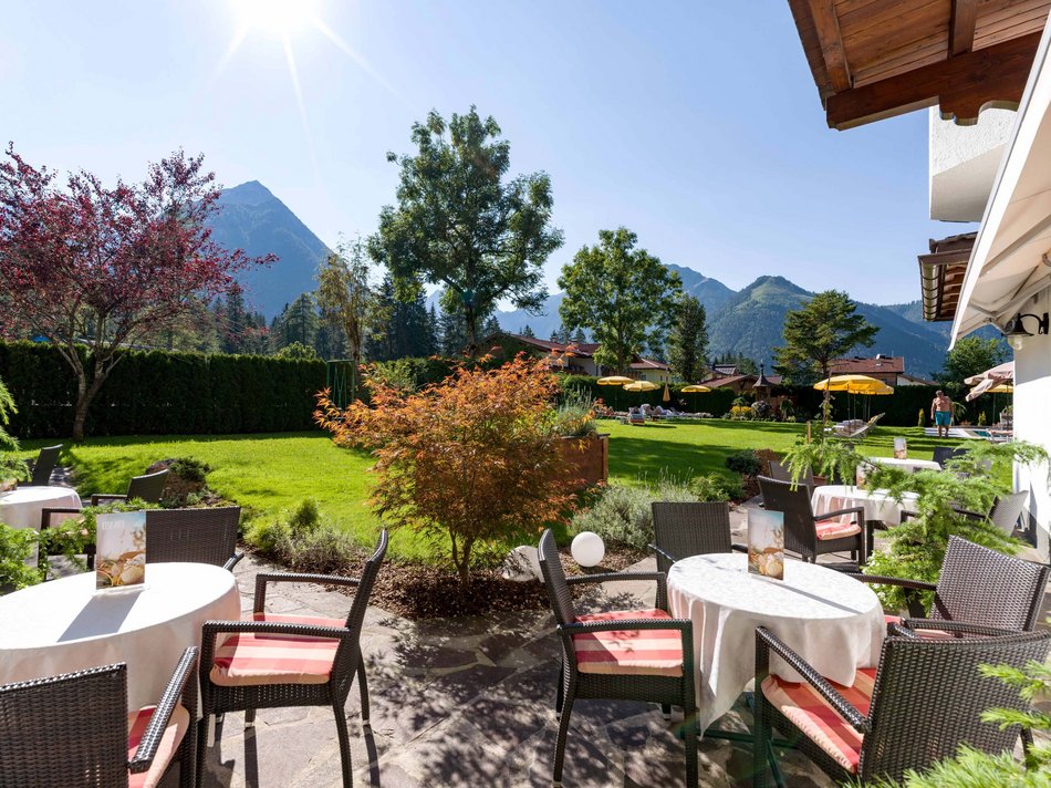 Das Hotel Karlwirt: herzlich willkommen! Sonnige Terrasse mit Tischen, Stühlen und Bergblick im Garten