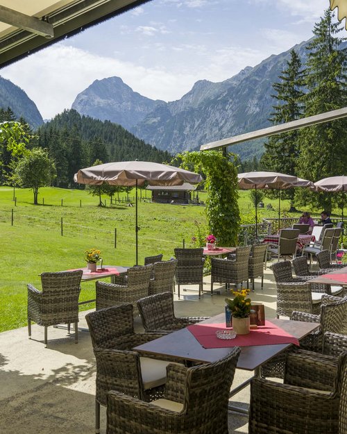 Das Hotel Karlwirt: herzlich willkommen! Terrasse mit Tischen und Stühlen vor Berglandschaft mit Wiesen und Bäumen