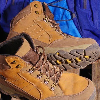 Das Hotel Karlwirt: herzlich willkommen! Braune Wanderschuhe mit blauem Rucksack auf Holzgitter