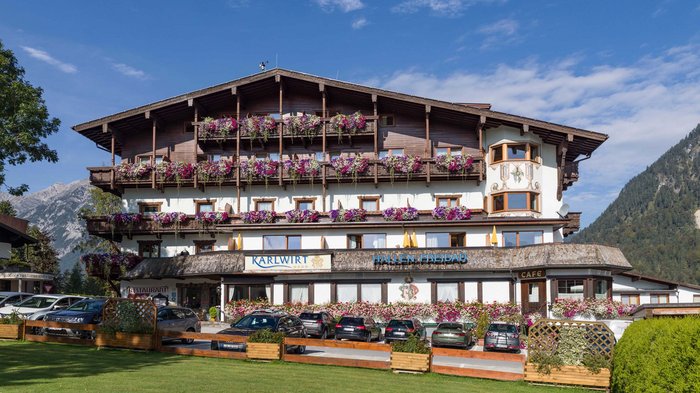 Das Hotel Karlwirt: herzlich willkommen! Hotelgebäude mit Blumenschmuck und Autos vor dem Eingang in den Alpen